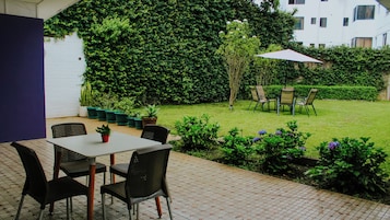 An outdoor patio with a table and chairs, surrounded by potted plants and a hedge.
