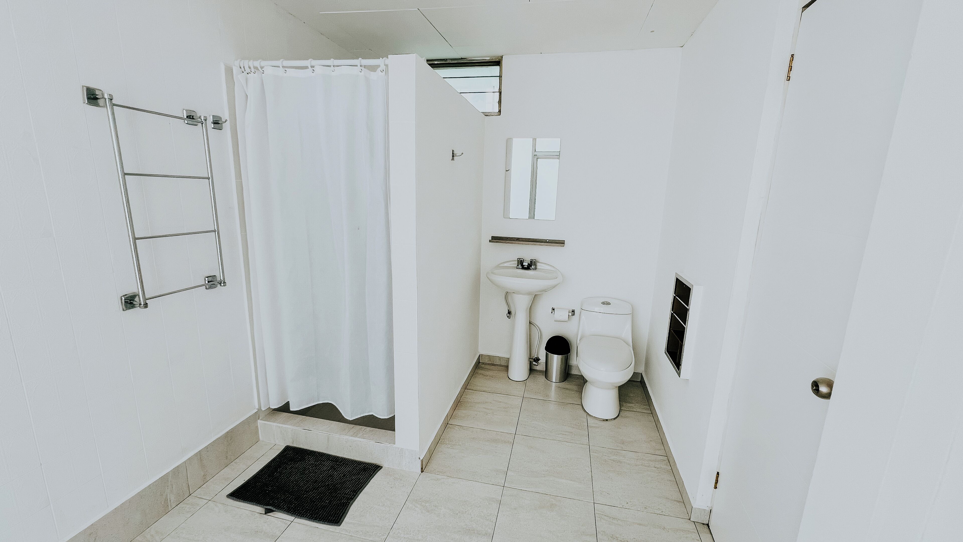 Een kleine, witte badkamer met douchegordijn, wastafel, toilet en een metalen handdoekhouder.