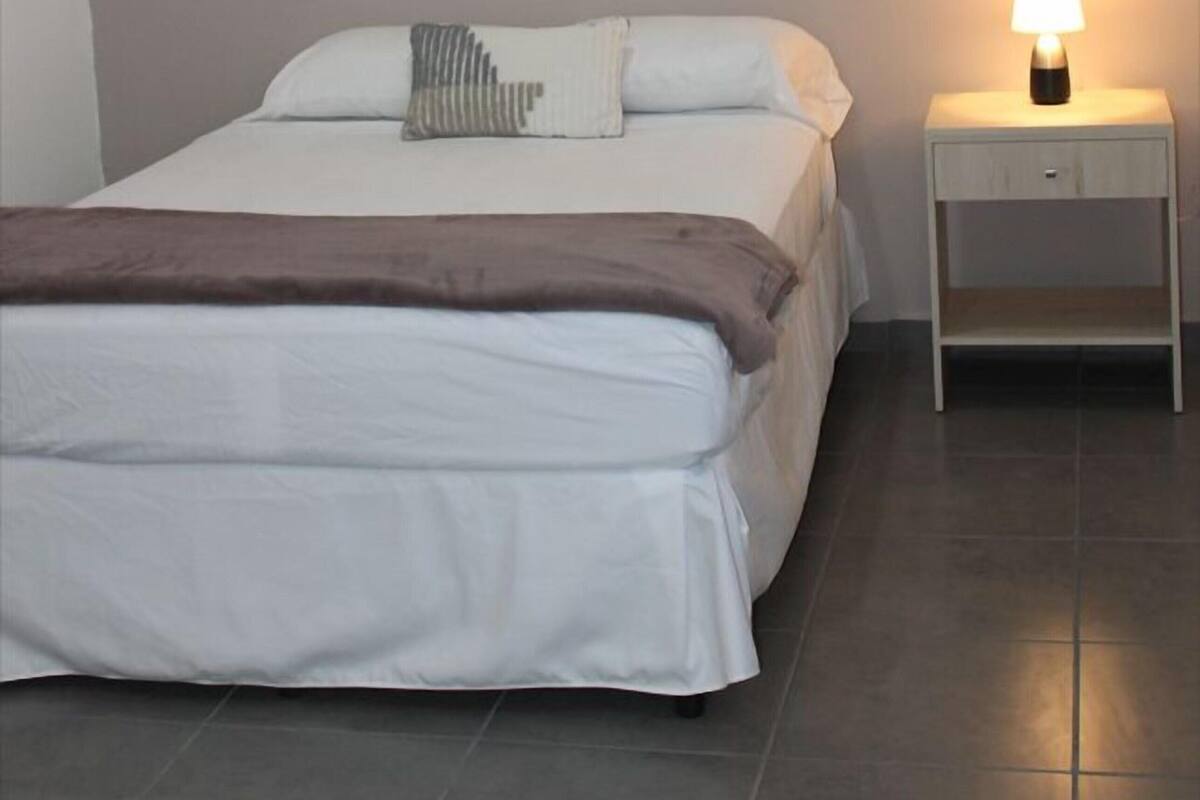 Un dormitorio con cama, una mesita de noche con lámpara e iluminación en el techo.