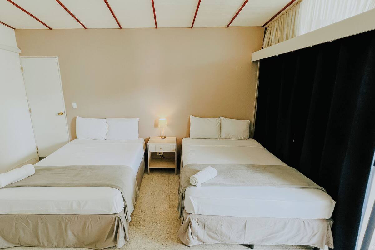 Una habitación de hotel con dos camas individuales, una mesita de noche con lámpara, una puerta y una cortina negra.