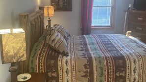 Een slaapkamer met een bed, een plafondventilator, een raam met gordijnen, een dressoir en een lamp.