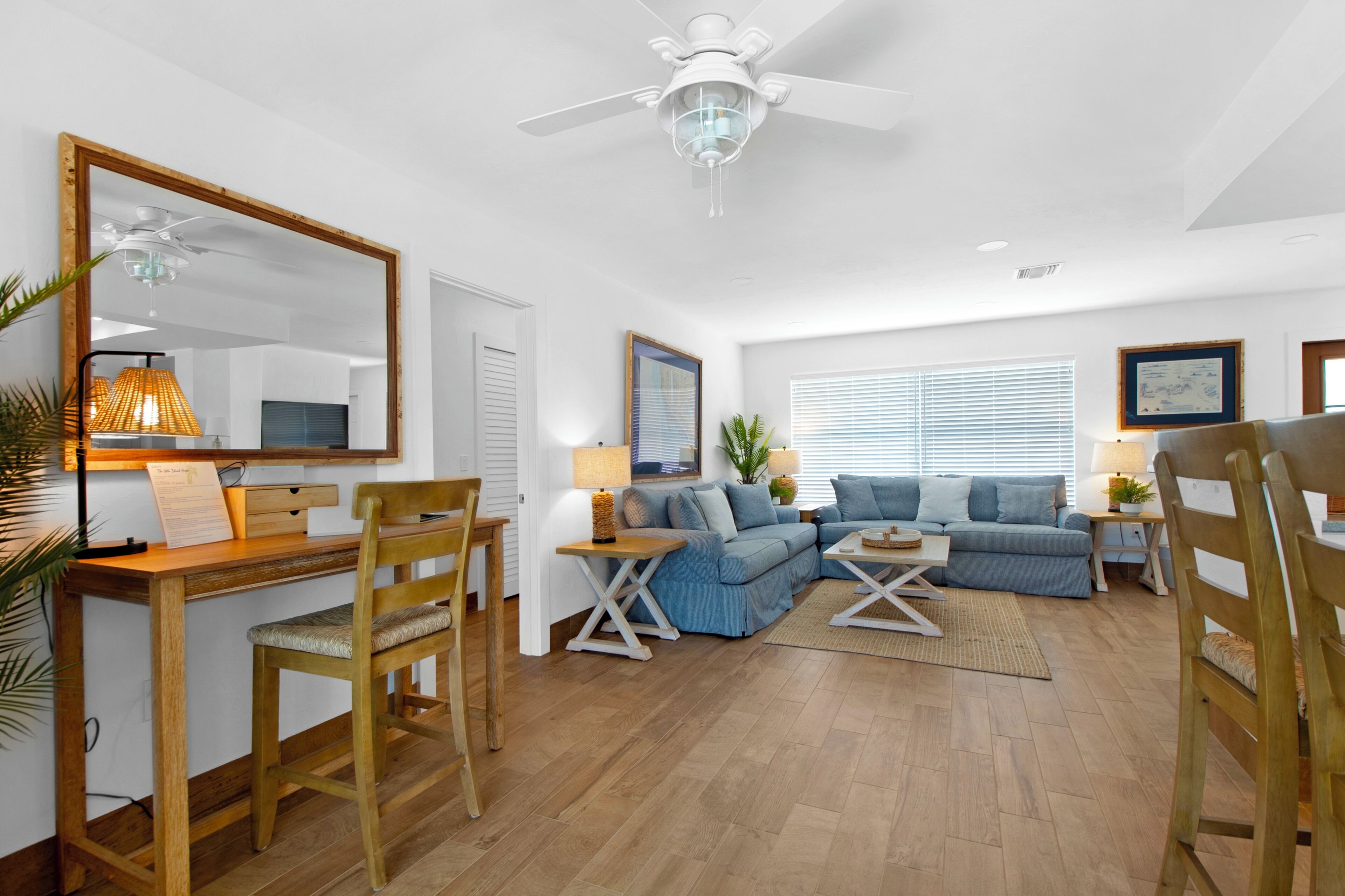 A spacious living room with a wooden desk, two blue sofas, a ceiling fan, and a large mirror.