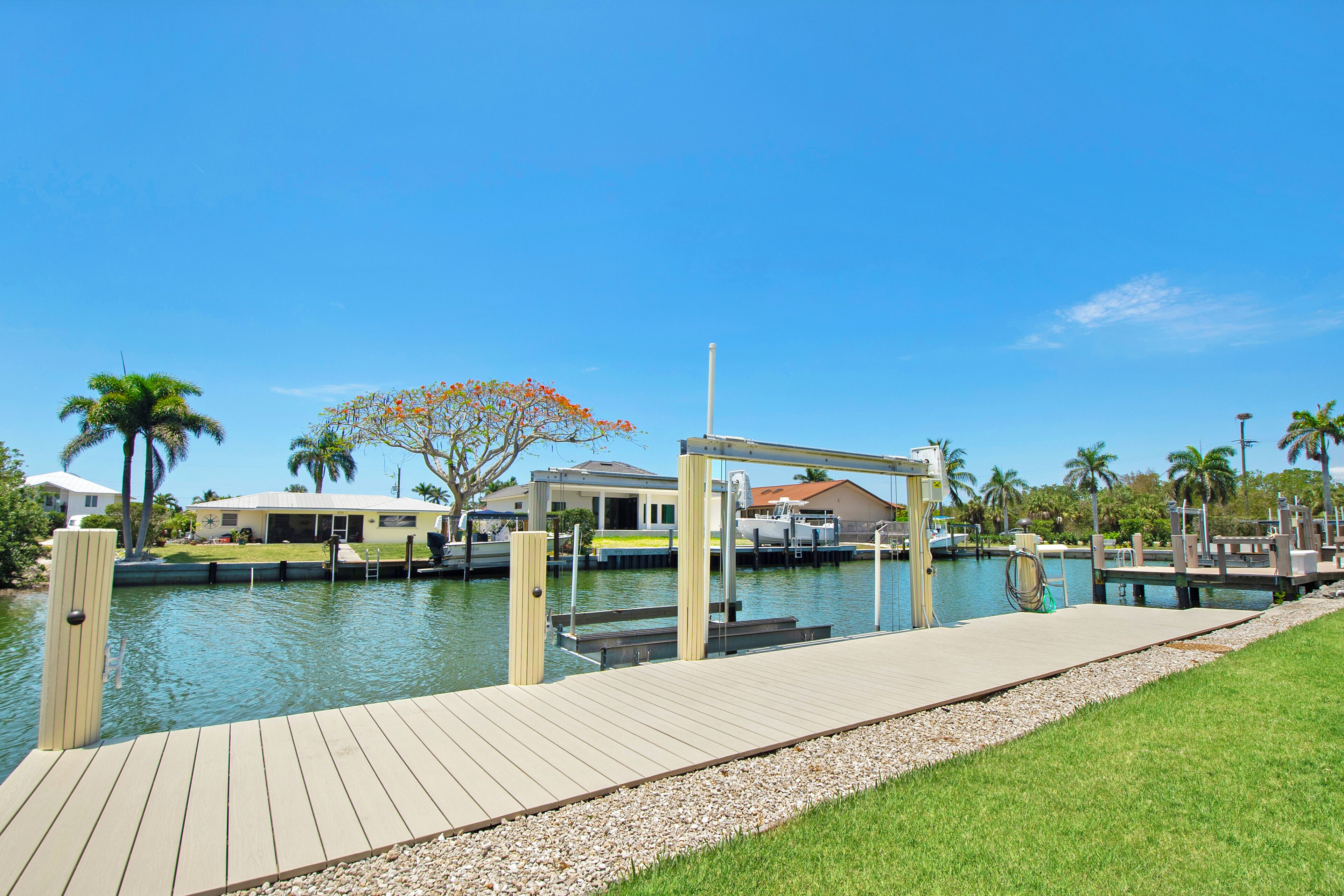A marina with a wooden dock, boats, and a house in the background.