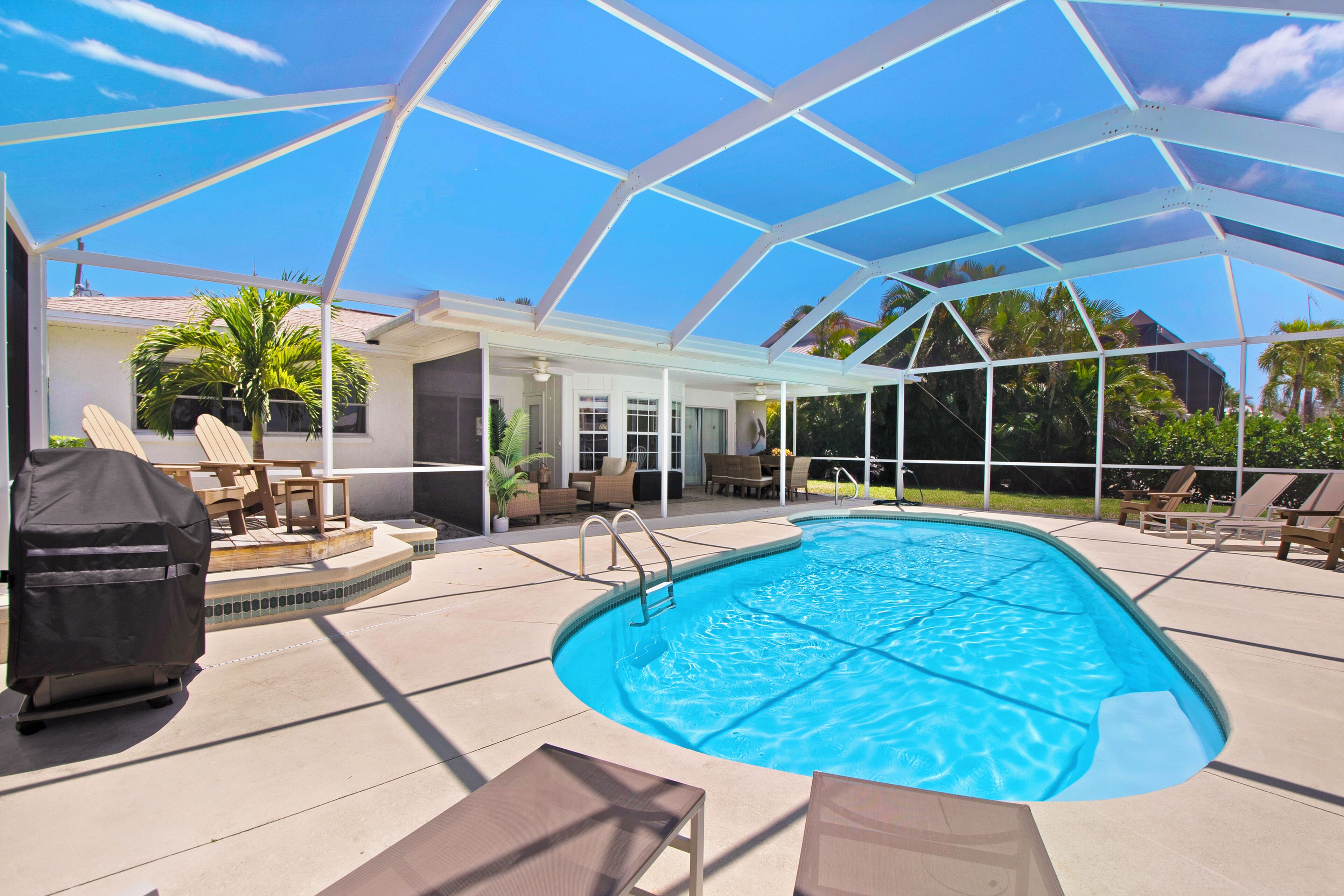 A covered outdoor swimming pool with lounge chairs and a barbecue grill.