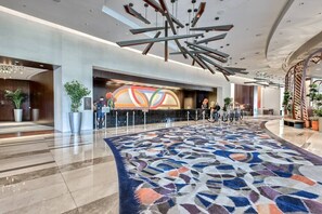 A modern hotel lobby with a large patterned carpet, a reception desk with a colorful abstract design, and a unique ceiling light fixture. - Vdara Studio Suite 011 * Pool View*Free Valet (Las Vegas)
