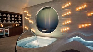 Ein moderner Wellnessbereich mit einer runden Whirlwanne, einem an der Wand befestigten Massagestuhl und einem Regal mit Kerzen.