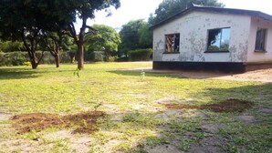 A grassy area with a small white building, possibly a house or a small structure, with a window and a door visible. - Backpacker's rest stop -10 min from downtown & a hike to the Falls!! (Livingstone)