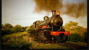 A steam locomotive with a large chimney emitting smoke, traveling on a railway track surrounded by greenery. - Backpacker's rest stop -10 min from downtown & a hike to the Falls!! (Livingstone)