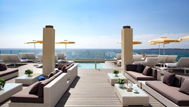 A rooftop lounge with sun loungers, umbrellas, and a pool.