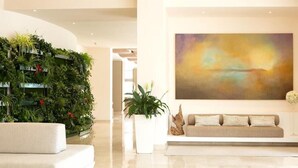 A modern living room with a white sofa, a large abstract painting, a green vertical garden, and a potted plant.