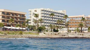 A coastal hotel with multiple floors, balconies, and palm trees.