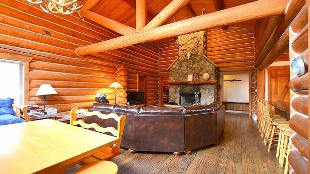 A log cabin interior with a stone fireplace, wooden furniture, and a cozy seating area.