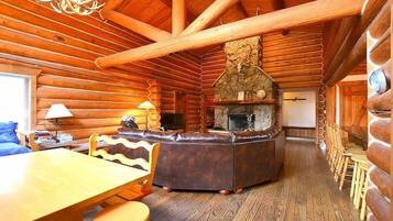 L’intérieur d’une cabane en rondins, avec une cheminée en pierre, des meubles en bois et un coin salon confortable.