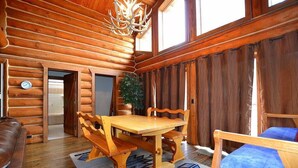 A log cabin interior with a wooden dining table, benches, a sofa, and a chandelier.
