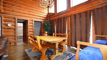 L’intérieur d’une cabane en rondins, avec une table à manger en bois, des bancs, un canapé et un lustre.