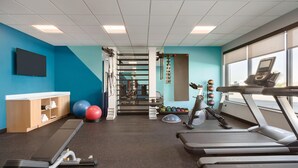 Un gimnasio con cintas de correr, pelotas de ejercicio y un soporte para pesas.