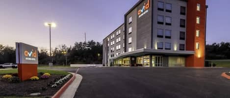 A modern hotel building with a flat roof, multiple windows, and a sign indicating it is the Avid Hotel.