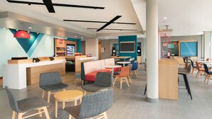 Un moderno vestíbulo de hotel con zonas de estar, un mostrador de recepción y un mostrador de restaurante visible.