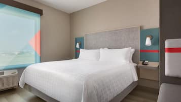 Una habitación de hotel moderna con una cama grande, una mesita de noche con lámpara y vistas al exterior.