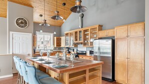 A kitchen with wooden cabinets, a stainless steel refrigerator, and a wooden island with bar stools. - Ocean Bliss — Coastal Retreat on Skagit Bay (La Conner)