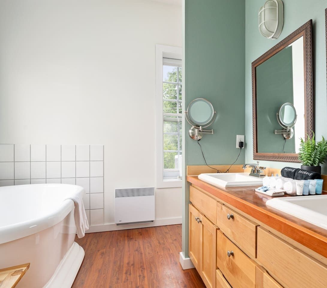 Un baño con bañera, tocador con espejo, ventana y radiador.