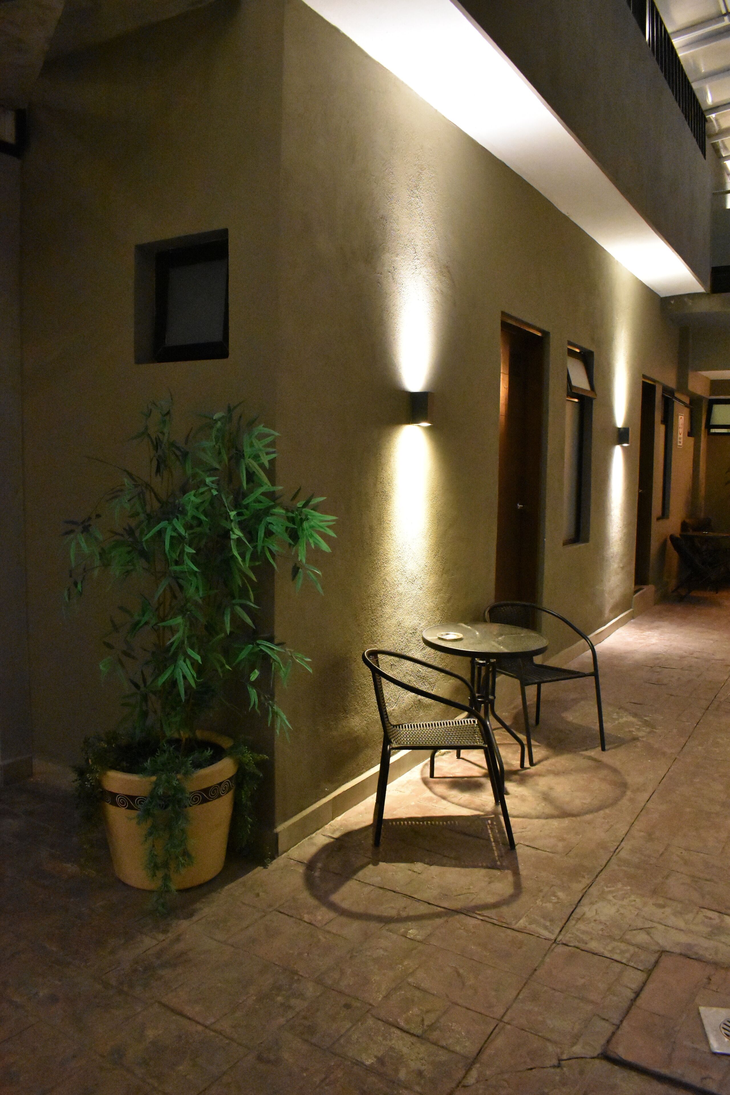 Un pasillo con una planta en maceta, una mesa con sillas y una lámpara en la pared.