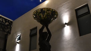 Eine Statue einer Figur, die eine Laterne hält, vor einer Gebäudefassade mit zahlreichen Fenstern und einer Lichterkette.