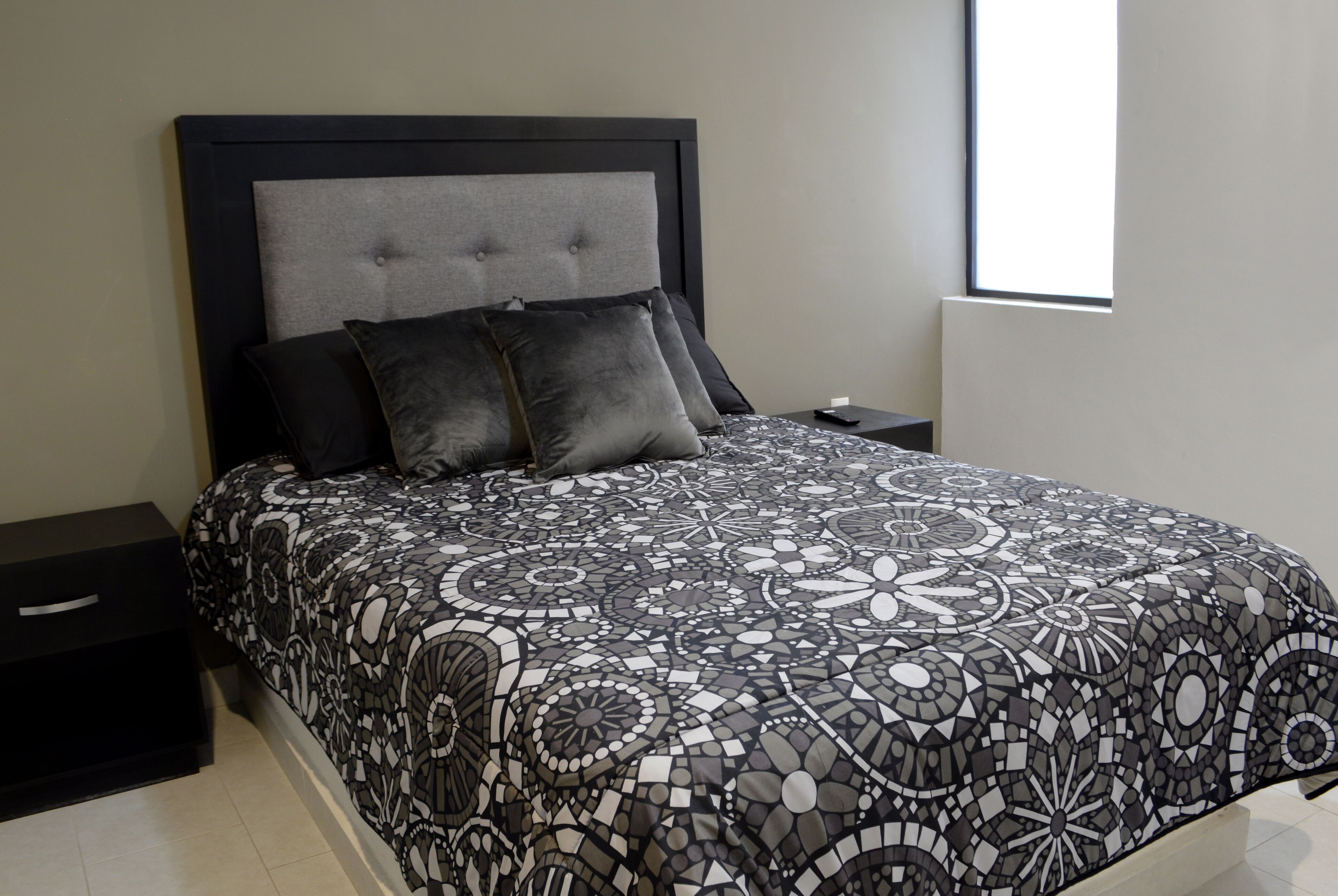 A modern bedroom with a large bed, a nightstand, and a window.