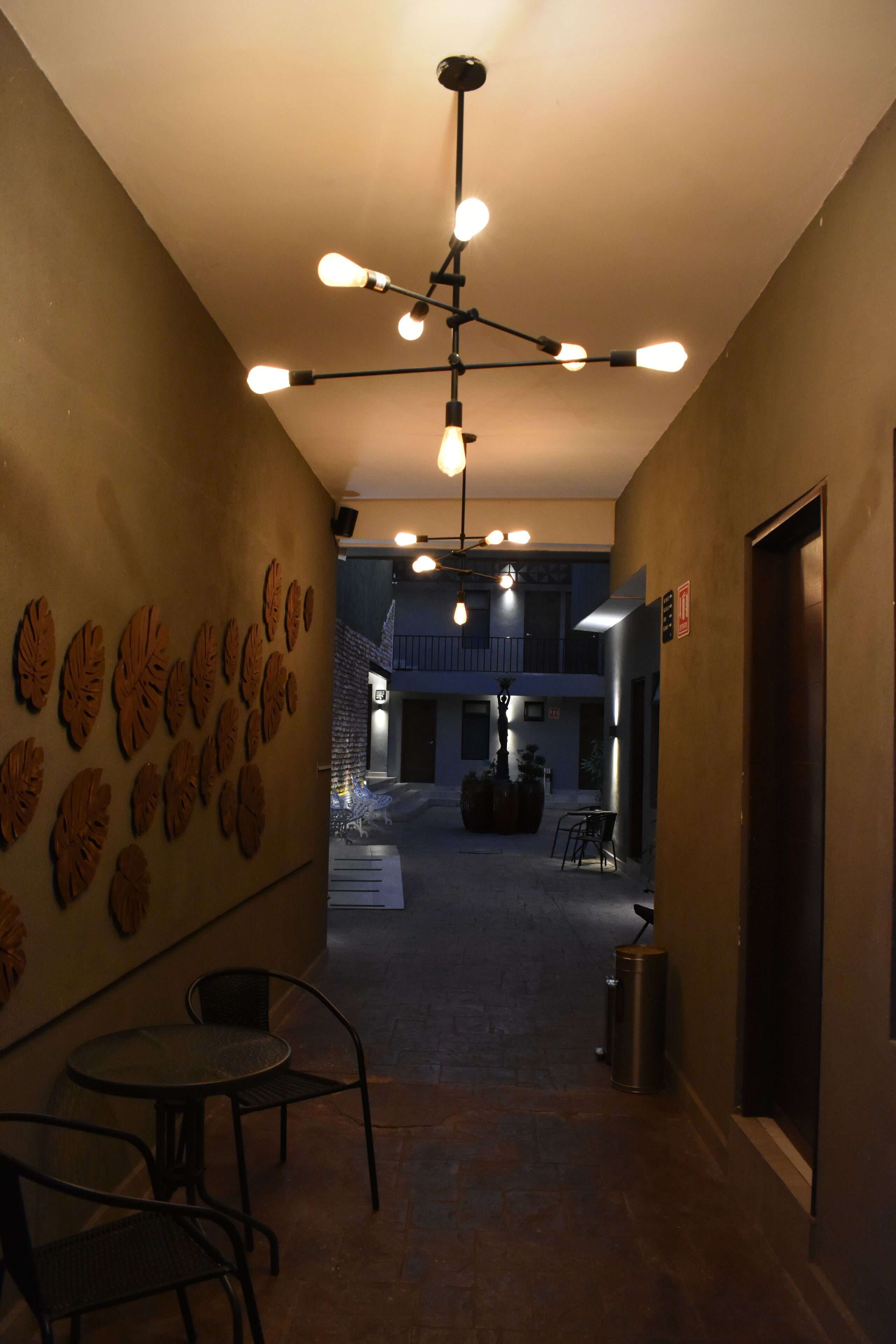 A corridor with a ceiling light fixture, a wall with leaf-shaped decorations, and a view of a building with a balcony.