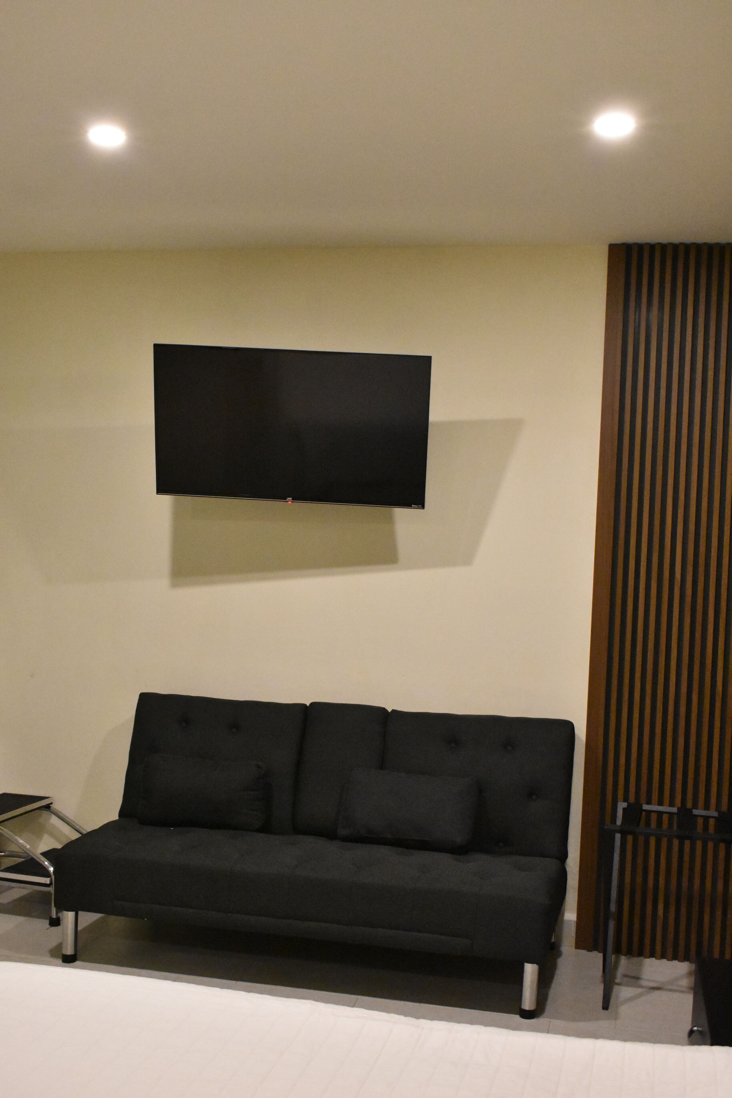 A modern living room with a black sofa, a flat-screen TV mounted on the wall, and a wooden panel on the right.