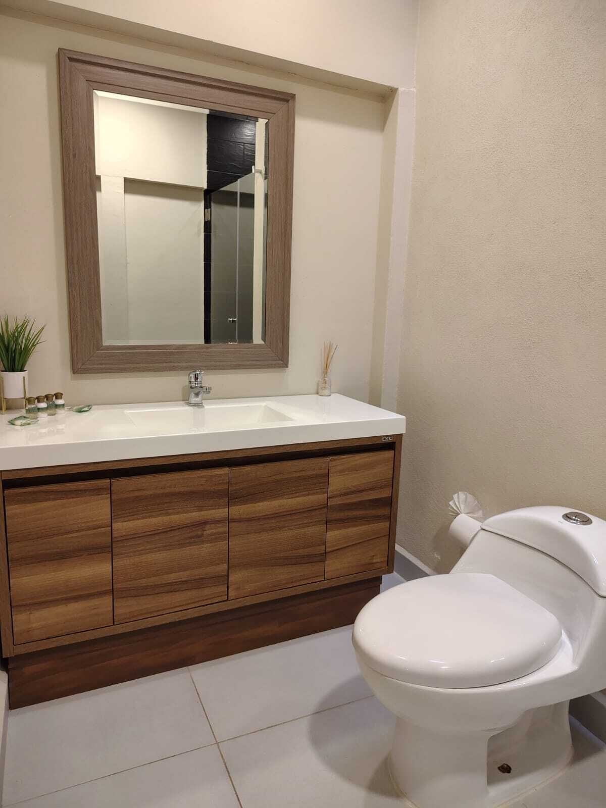 A bathroom with a wooden vanity, a white sink, a mirror, and a toilet.