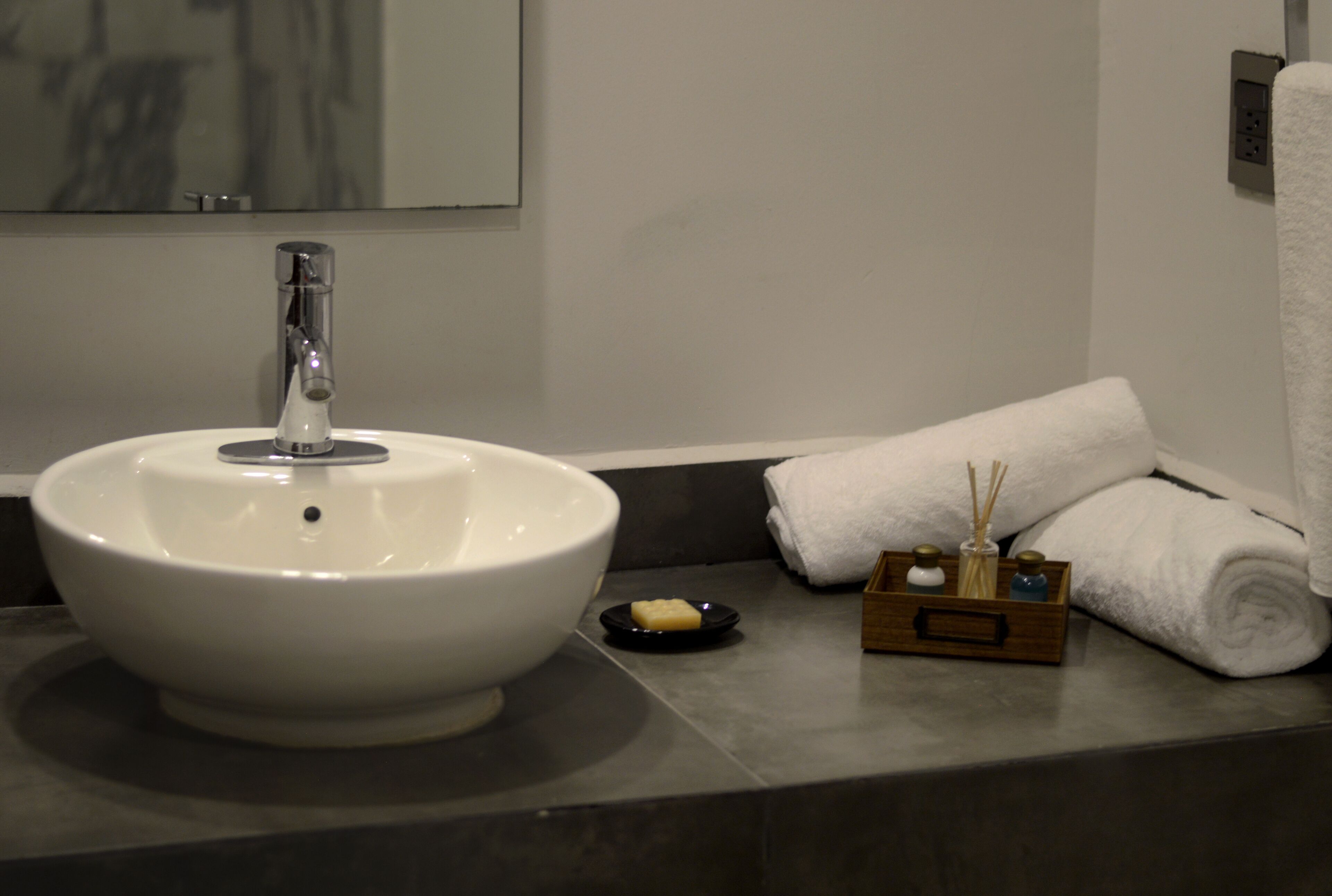A bathroom with a white sink, a mirror, a towel, and a tray with toiletries.