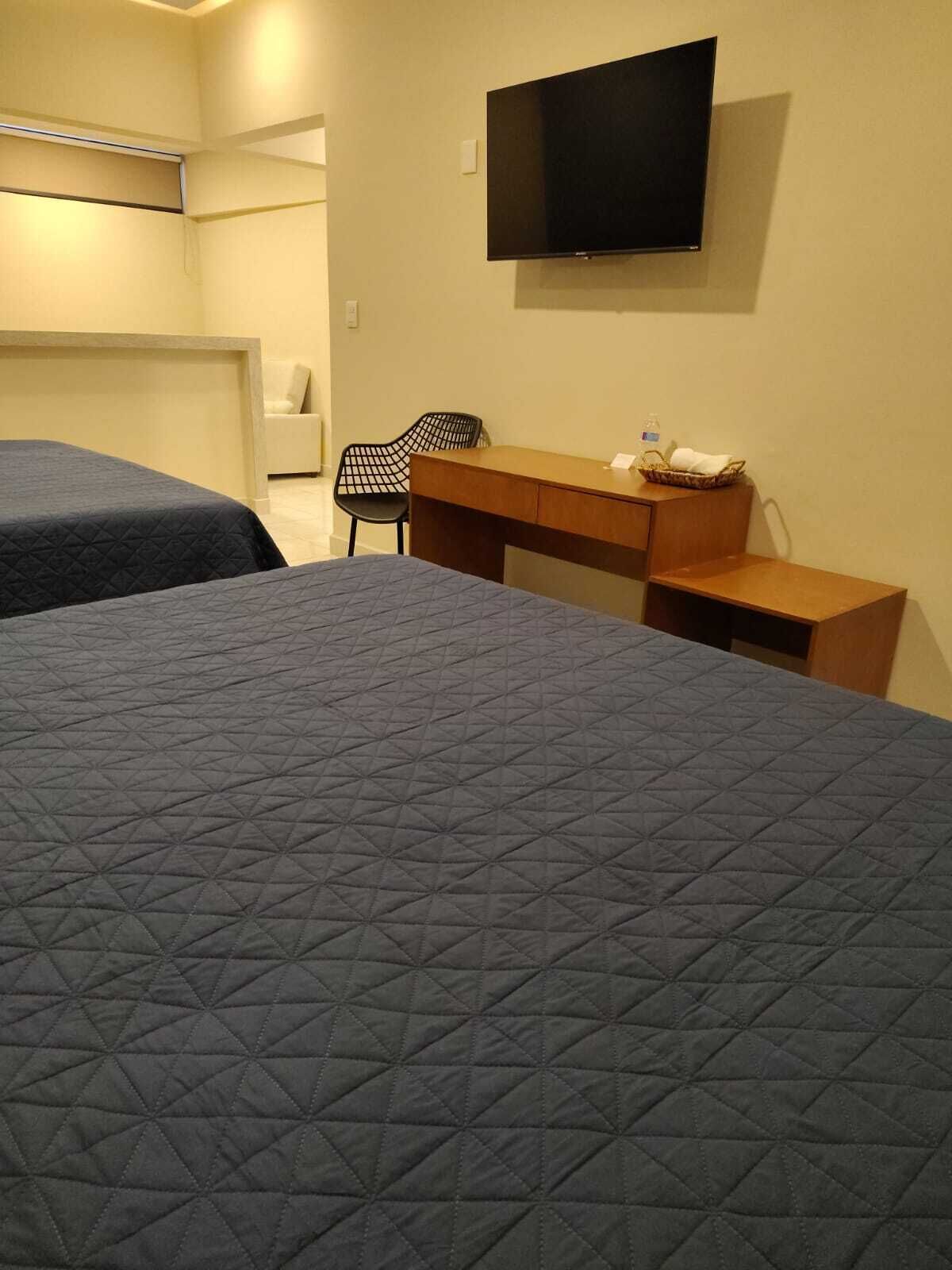 A hotel room with two beds, a desk, a chair, and a TV mounted on the wall.