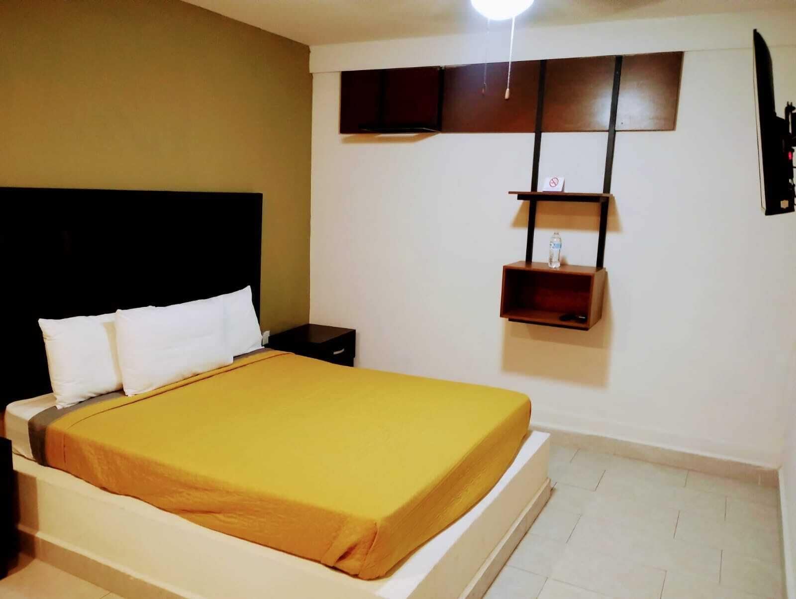 Een hotelkamer met een groot bed, een nachtkastje, een wandplank met een fles en een plafondlamp.