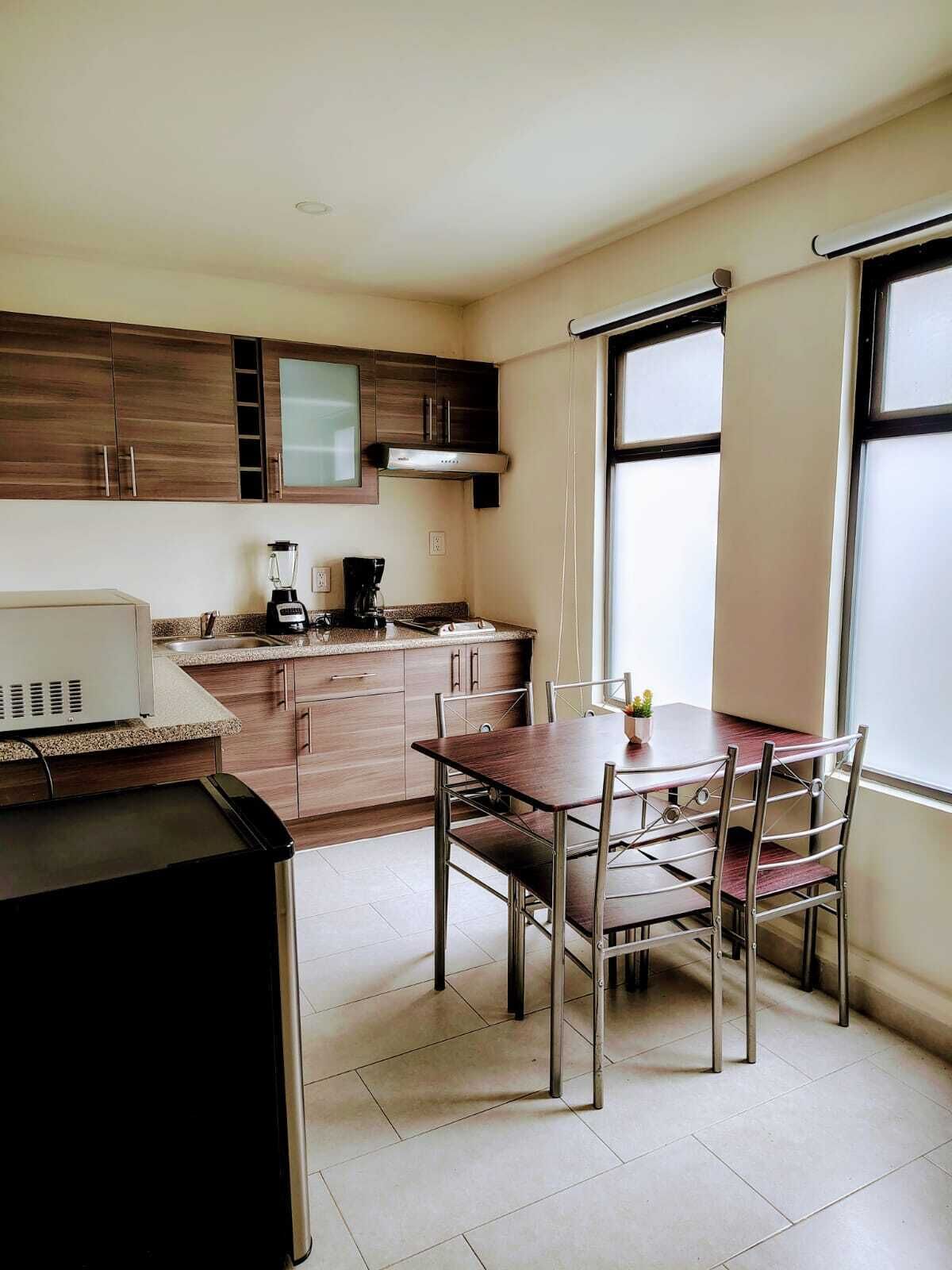 A compact kitchen with wooden cabinets, a built-in oven, a coffee maker, and a dining table with chairs.