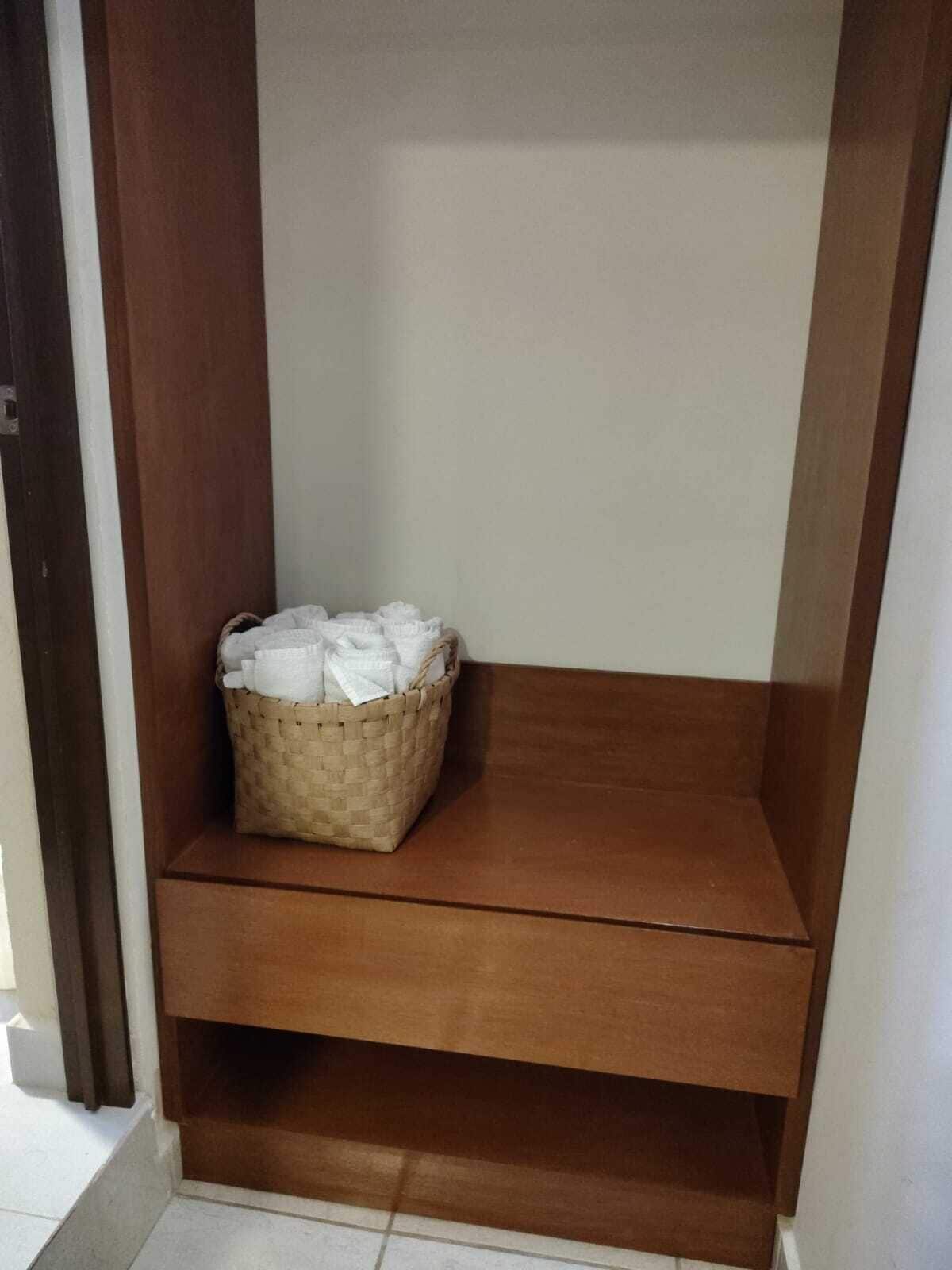 A corner of a room with a wooden shelf and a woven basket containing white items.