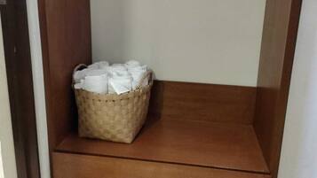 A corner of a room with a wooden shelf and a woven basket containing white items.