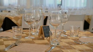 Una mesa de comedor dispuesta con copas de vino, vasos de agua y cubiertos, con un atril para el menú en una pizarra en el centro.