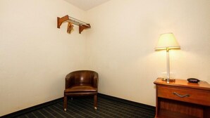 Una habitación de esquina con una silla de madera, una mesita de noche con una lámpara y una estantería en la pared.