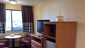 Habitación de hotel con cama, escritorio con silla, televisor, refrigerador y ventana con cortinas.