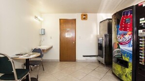Una habitación pequeña con una puerta que dice “Privado”, una mesa con sillas, un refrigerador y una máquina expendedora.