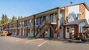 Un motel con una escalera central, varias habitaciones y un estacionamiento.