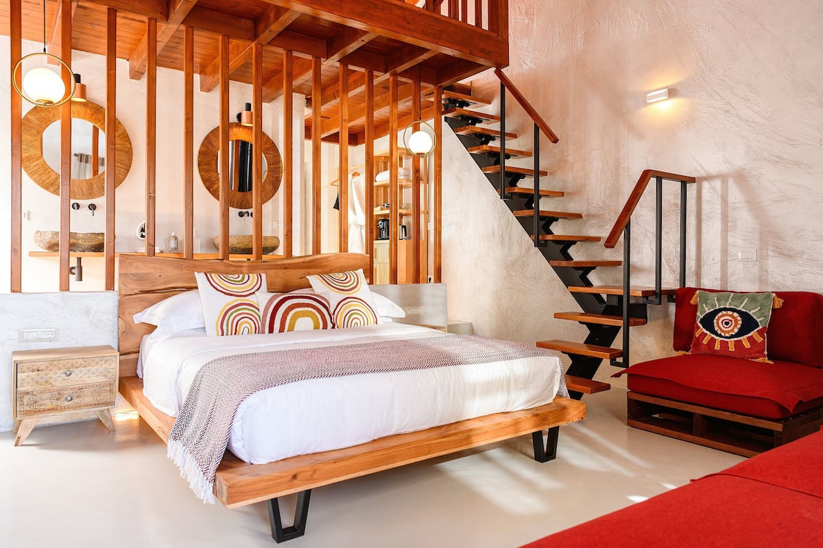 Un dormitorio con una cama de madera, una silla roja, una escalera y un espejo grande.