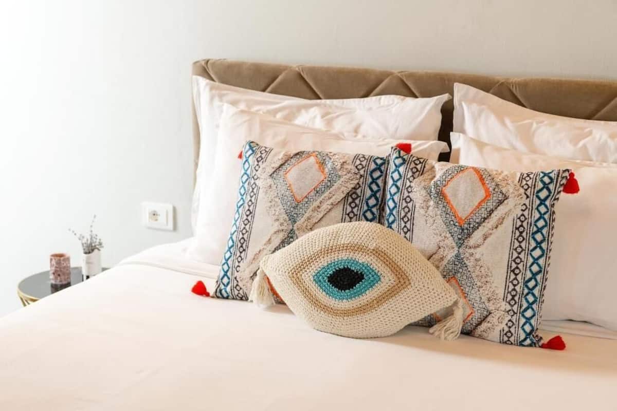 Una cama con ropa blanca, dos almohadas estampadas y un adorno de crochet.