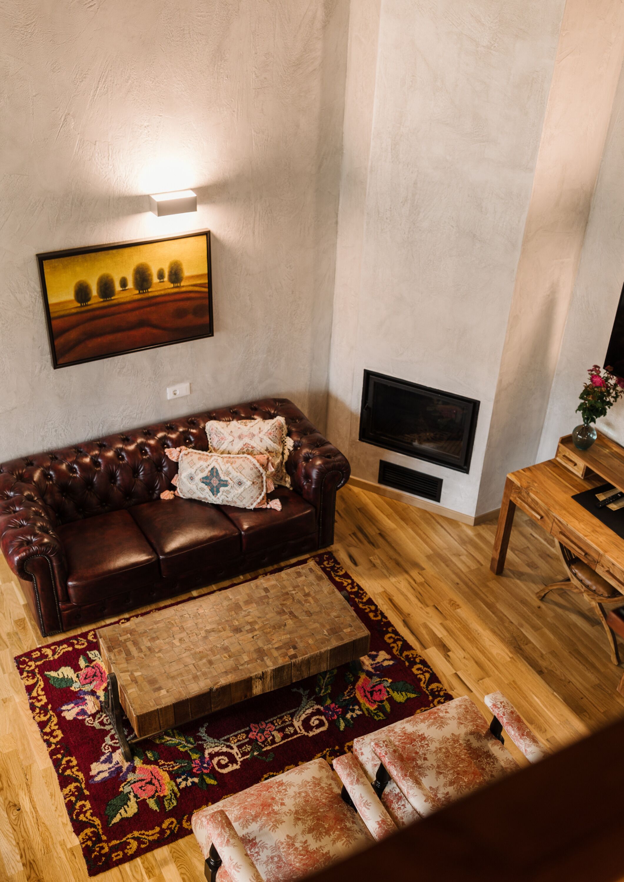 A living room with a brown leather sofa, a wooden coffee table, a TV mounted on the wall, and a small wooden side table with a vase.