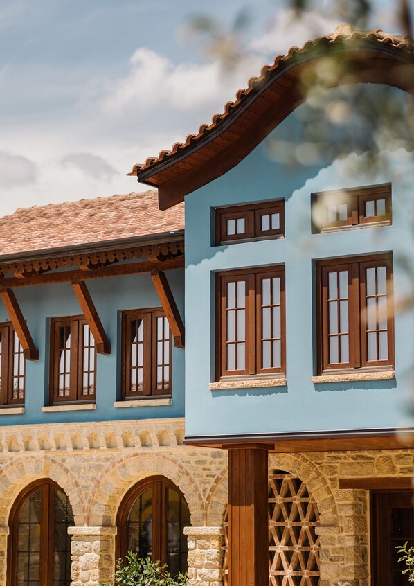 A building with a blue facade, stone arches, and wooden window frames. - Blerina's Village Project  (Kamëz)