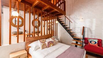 A bedroom with a wooden headboard, a bed with white bedding, a red sofa, a staircase, and a circular mirror on the wall.