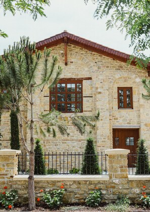 A stone building with a wooden door and windows, surrounded by a stone wall and a small tree. - Blerina's Village Project  (Kamëz)