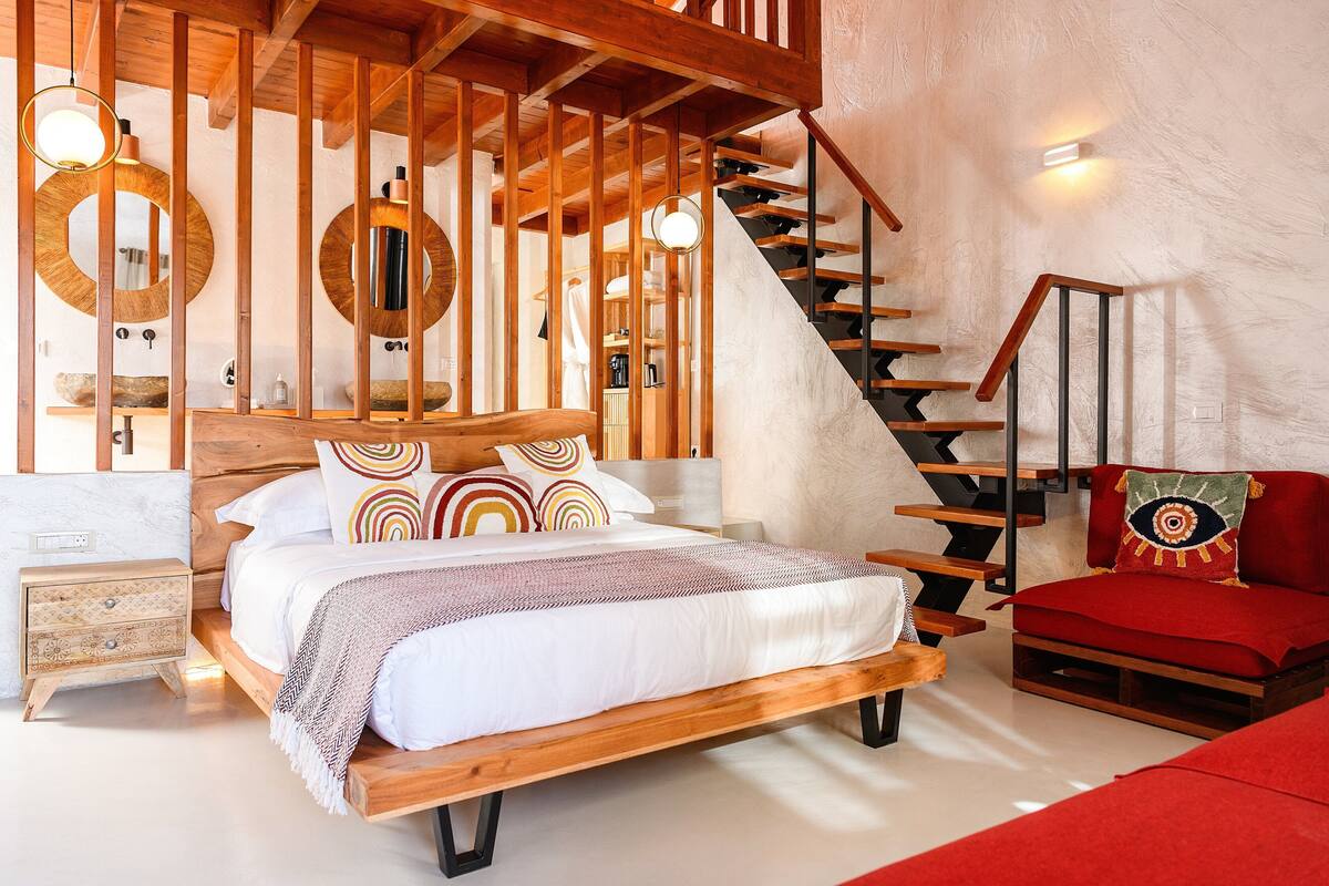Un dormitorio con una cama de madera, una silla roja, una escalera y un espejo grande.