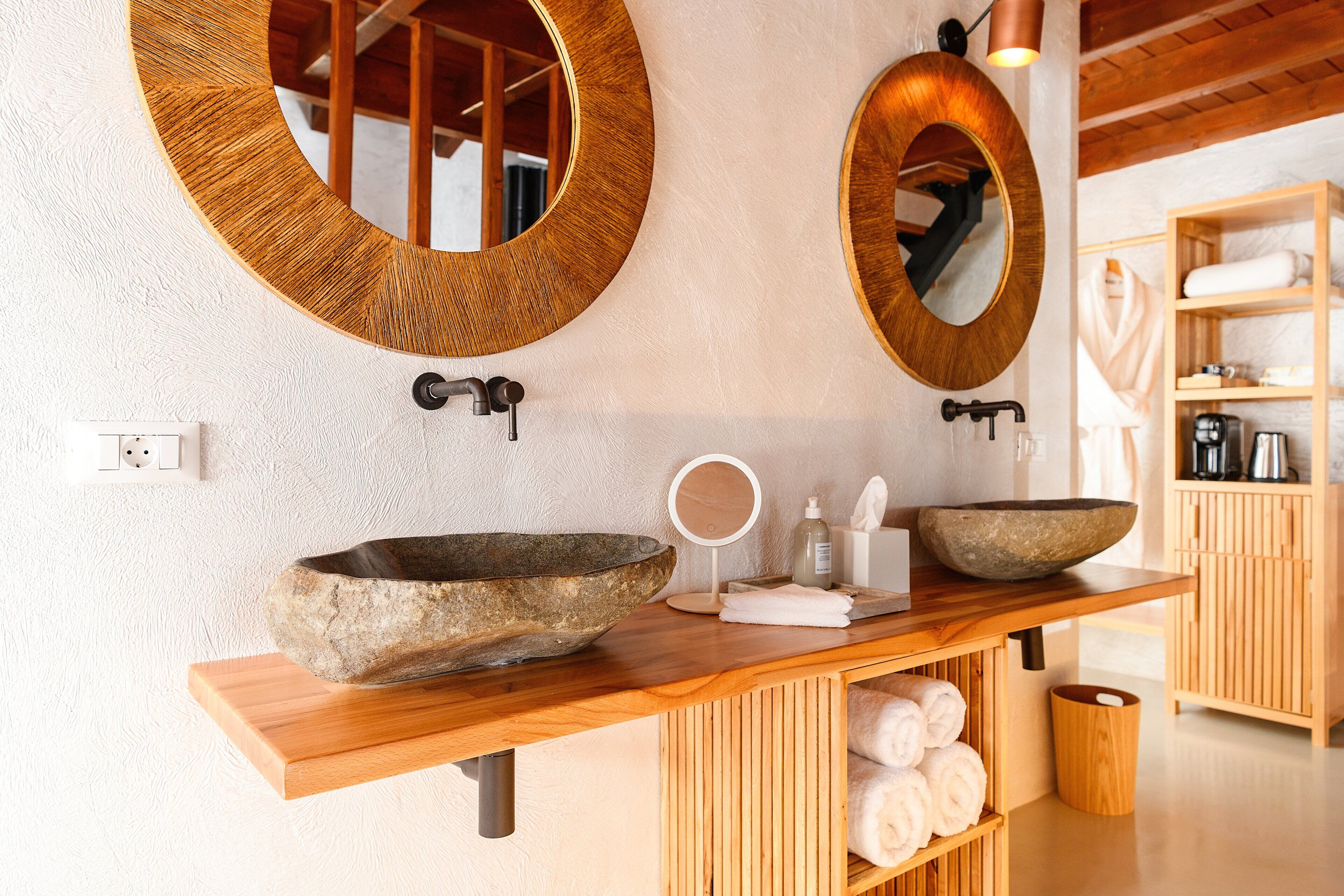 A bathroom with two large wooden-framed mirrors, a stone basin, a wooden vanity, and a towel rack with neatly folded towels.